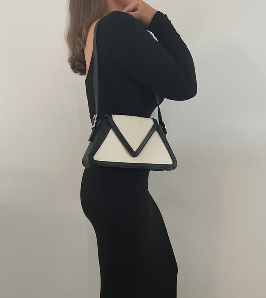 Cream canvas shoulder bag with black trim, triangular flap, silver buckle hardware and an adjustable black strap