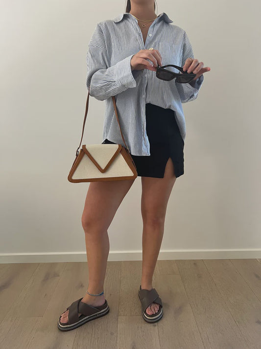 Tan structured shoulder bag with a triangular flap, silver buckle hardware and adjustable strap, with a vegan leather border