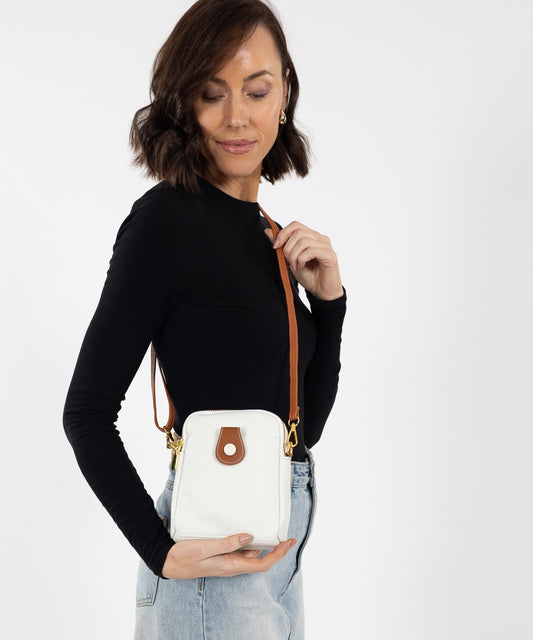 White pebbled leather crossbody bag with tan trim, gold-tone hardware, front slip pocket, rounded top and tan strap