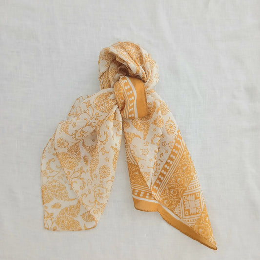 Cream silk scarf with gold paisley print and a gold border, shown with a soft sheen and elegant drape