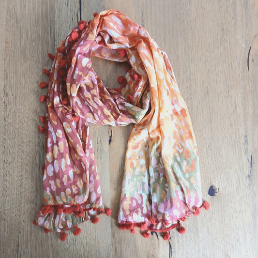Orange and sea green cotton scarf with small pom-poms along the edges, laid out to show its long rectangular shape