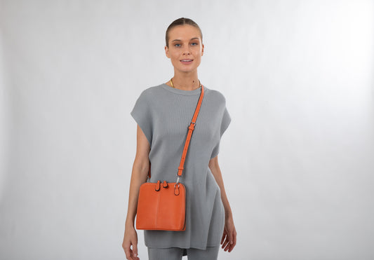 Compact vegan cross-body bag in polyurethane with gunmetal hardware, kissing zips and highlighted stitching on the front